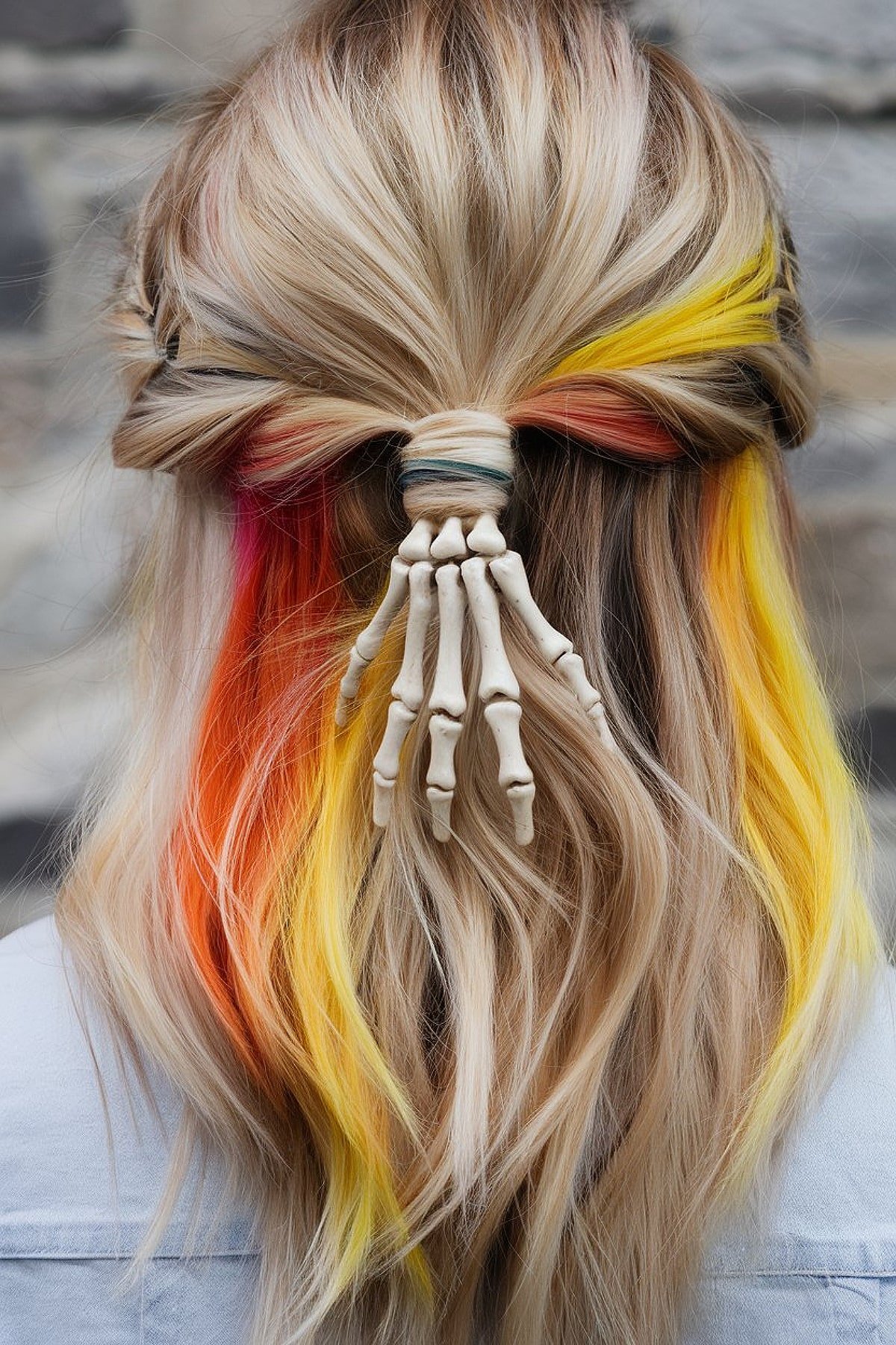 Blonde hair with colorful streaks in yellow, orange, and pink, styled with a skeleton hand clip